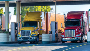 Different big rigs semi trucks standing on fuel station for truck refueling and continuation of the route