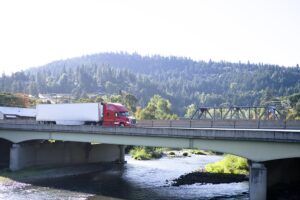 Modern big rig semi truck with semi trailer moving on the bridge across mountain river