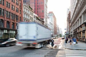 Busy view of 23rd Street with delivery truck speeding past the people walk down the sidewalk in New York City