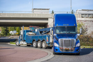 Big rig tow truck towing broken blue big rig semi truck tractor going under the bridge
