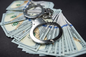 Police handcuffs lie on many dollar bills isolated on black background.