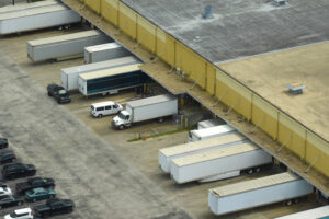 Top view of giant logistics center with many commercial trailer trucks unloading and uploading retail products for further shipment. Global economy concept