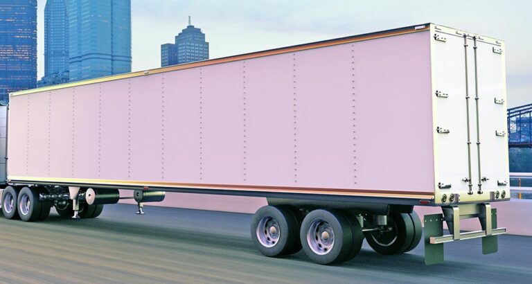A cargo truck on the road at dusk in front of a city skyline.