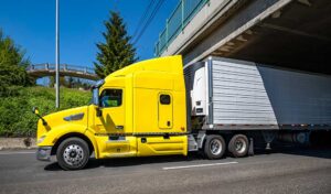 Yellow Tractor pulling refrigerated trailer beneath freeway overpass